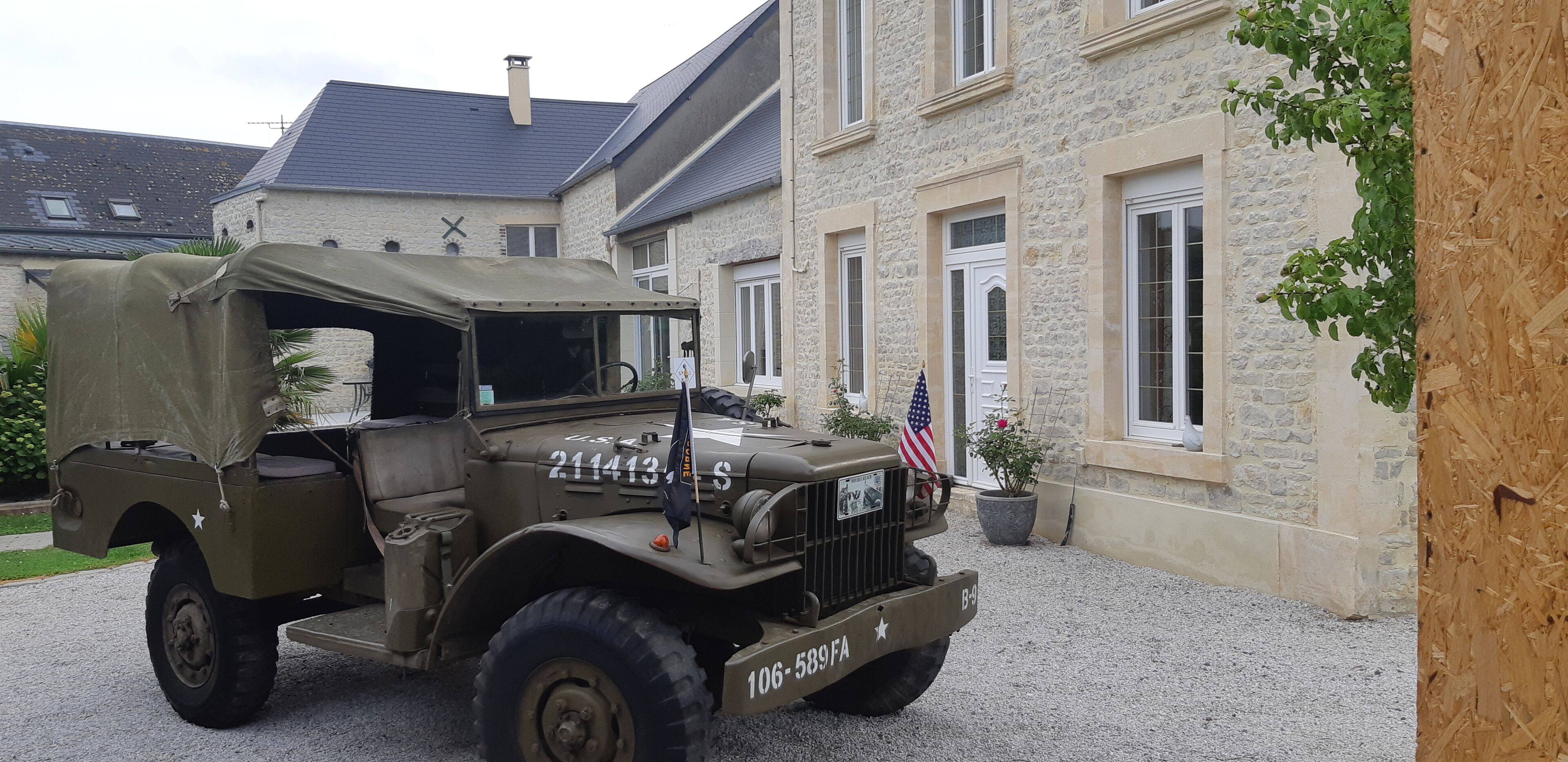 Un jeep militar antiguo estacionado frente a un edificio de piedra con una bandera.