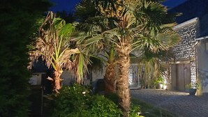 A garden with palm trees and potted plants in front of a building with a stone wall and a wooden door. - Townhouse 12 persons LE DOMAINE DES PAONS 4 ETOILES (Saint-Germain-du-Pert)