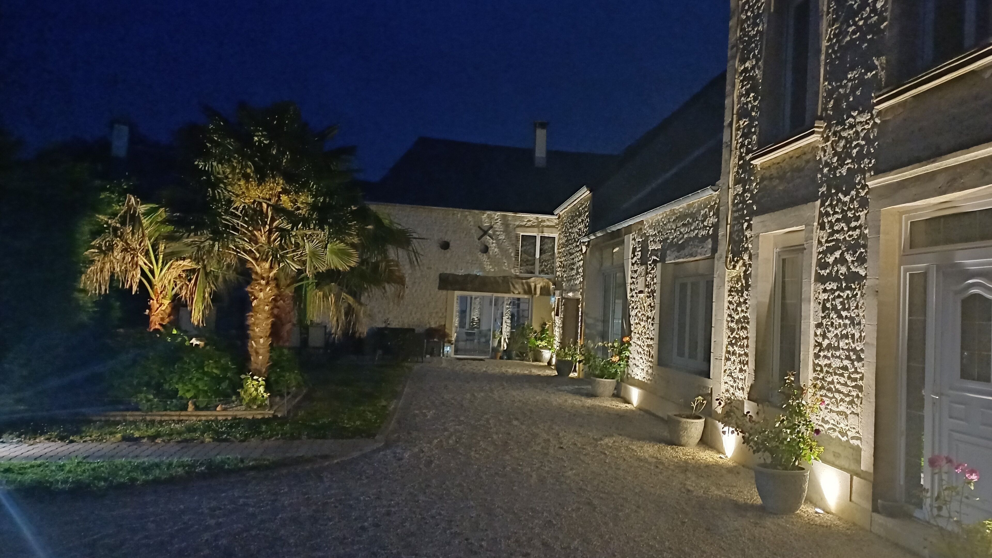 Een gebouw van steen met een grindpad, palmbomen en potplanten.