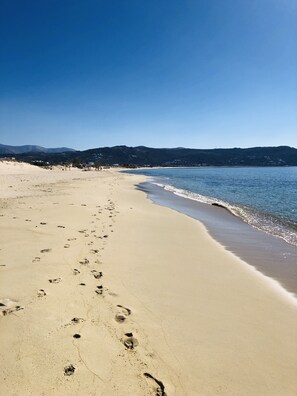 A beach with footprints leading to the water, a clear sky, and distant hills. - VILLA PERGOLA, a private villa with a private pool and an incredible view. Quiet neighborhood. (Naxos)