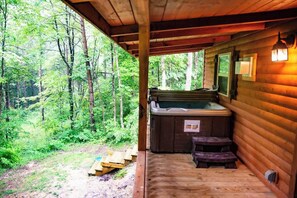 Eine Holzhütte mit Whirlpool, Holzstufen und Blick auf einen Wald.