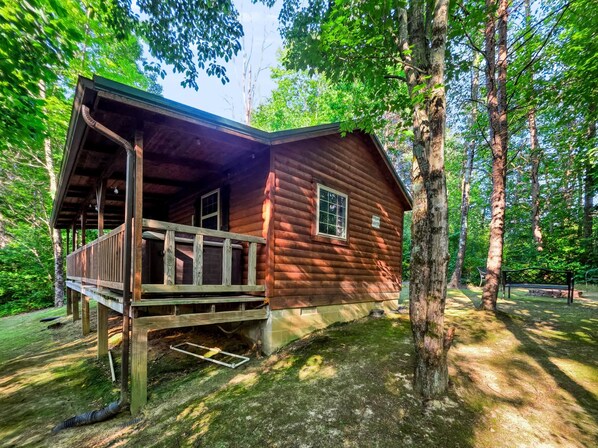 A wooden cabin with a porch, surrounded by trees.