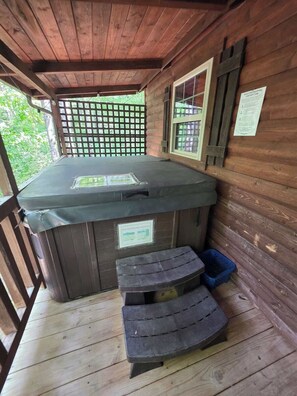 A hot tub on a wooden deck with a wooden ceiling and walls, a window, and a sign with instructions.