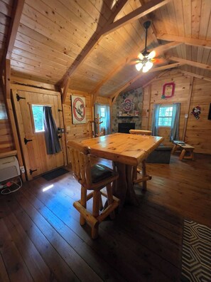 Ein Holzblock-Interieur mit Esstisch, Stühlen, Kamin und Deckenventilator.