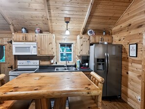A wooden cabin kitchen with a wooden table, a stove, a microwave, a sink, and a refrigerator.