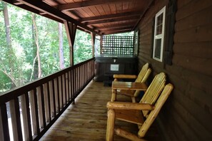 A wooden cabin with a porch, a fireplace, and a view of the forest. - Buckeye Hut at Avenwood Cabins (new straitsville)
