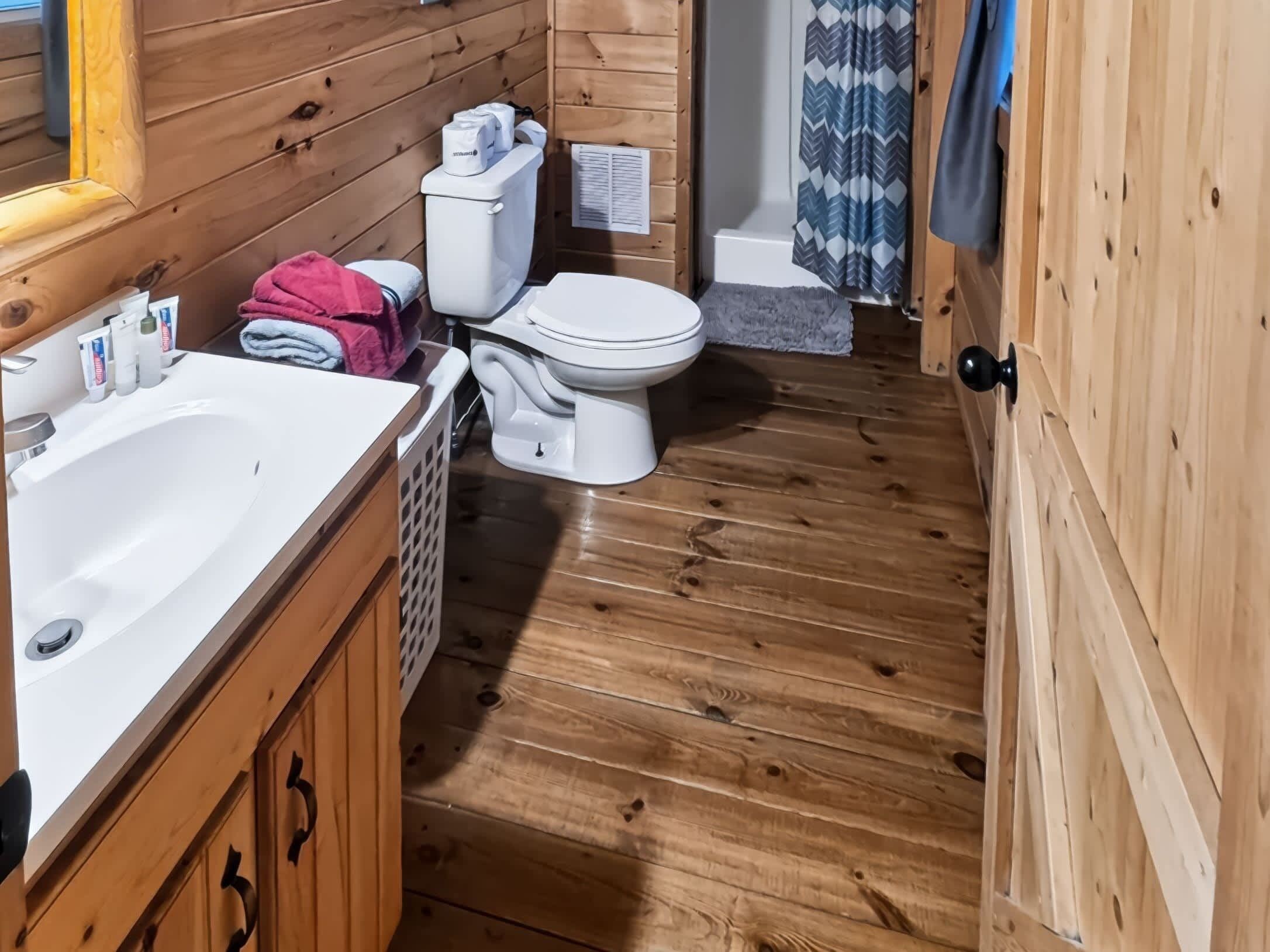 Ein Badezimmer einer Holzhütte mit Waschbecken, Toilette und Duschbereich, alles in Weiß.