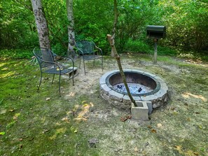 A fire pit surrounded by chairs and a mailbox in a wooded area.