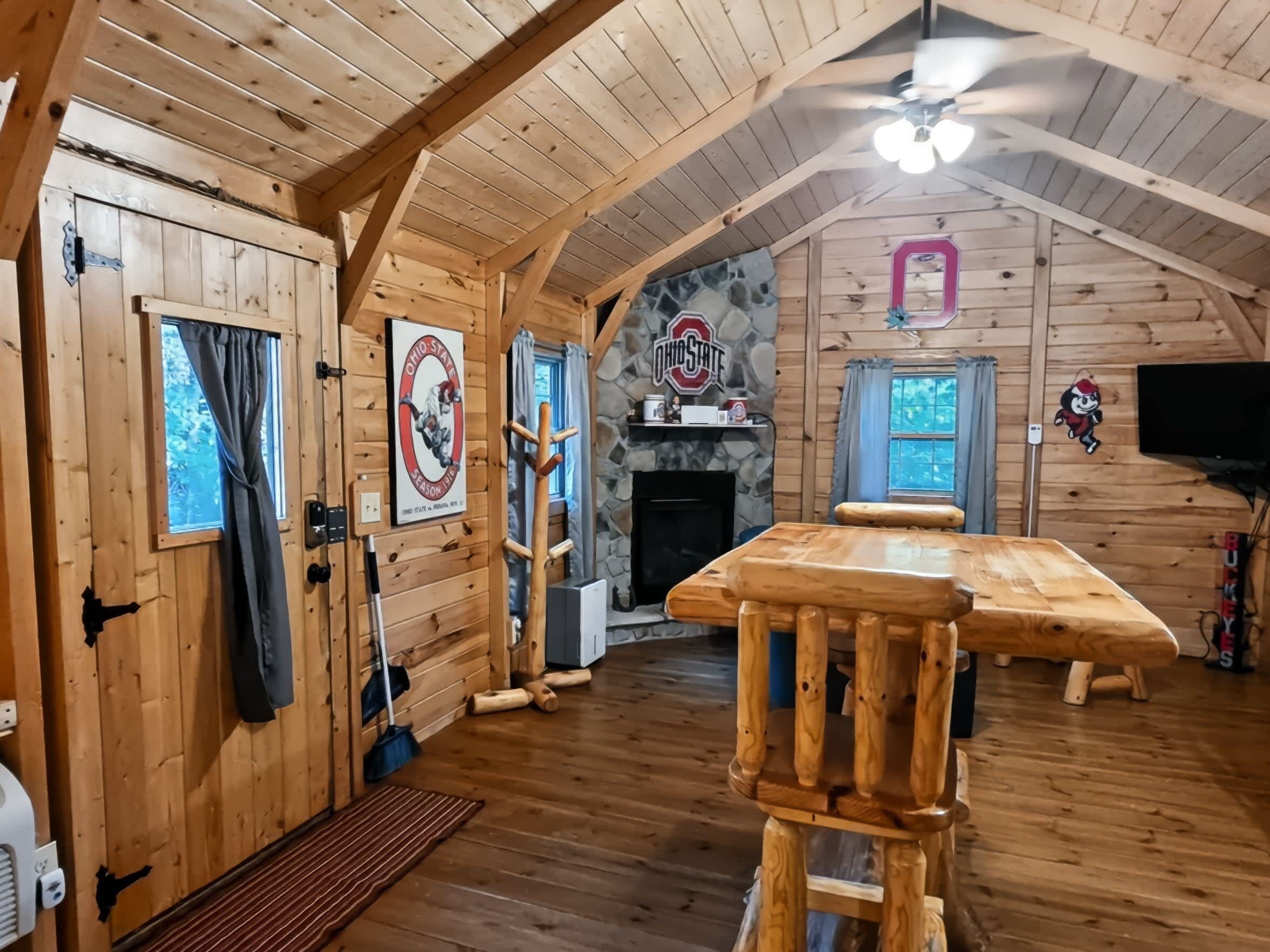 A log cabin interior with a wooden dining table, a fireplace, and a stone wall with an Ohio State logo.