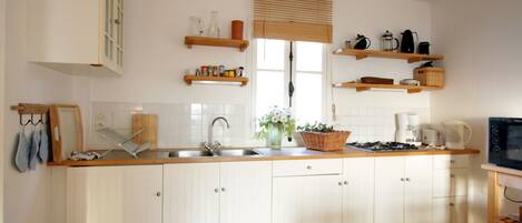 Una cocina con armarios blancos, encimera de madera, un fregadero y una estufa. Hay repisas sobre la encimera con varios utensilios de cocina.