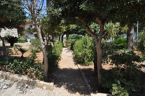 Un sendero bordeado de árboles y arbustos, que conduce a un edificio con fachada de piedra.