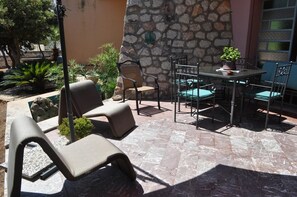 An outdoor patio with a stone wall, a table with chairs, and lounge chairs. - Villa Faro on the waterfront with a private garden (TRAPANI)