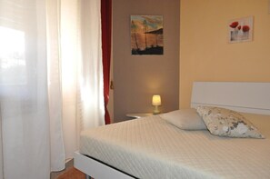A neatly made bed with a quilted cover, a bedside lamp, and a wall painting. - Villa Faro on the waterfront with a private garden (TRAPANI)