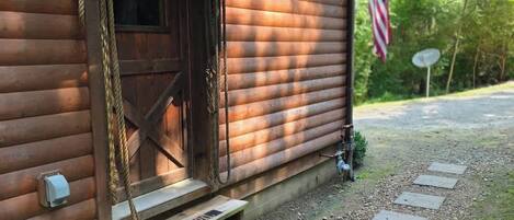 Una cabaña de madera con puerta principal, un pequeño porche y una bandera.