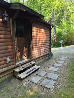 Una cabaña de madera con puerta principal, un pequeño porche y una bandera.