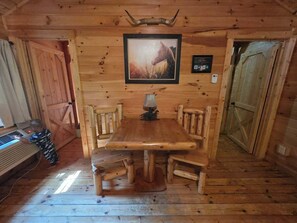 A wooden interior with a dining table, benches, a framed picture, and a door.