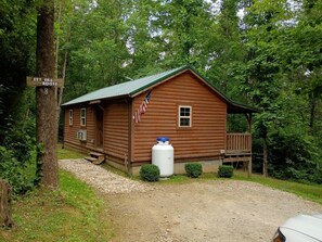 A rustic cabin with a porch, a flag, and a water tank.