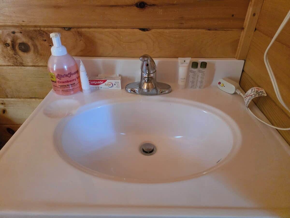 A bathroom sink with a wooden wall, a bottle of lotion, a box of soap, and a faucet.