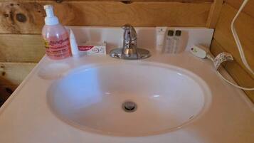 A bathroom sink with a wooden wall, a bottle of lotion, a box of soap, and a faucet.