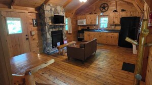Ein gemütliches Blockhaus-Interieur mit Kamin aus Stein, Holzmöbeln, einer Küche mit Mikrowelle und einem Deckenventilator.