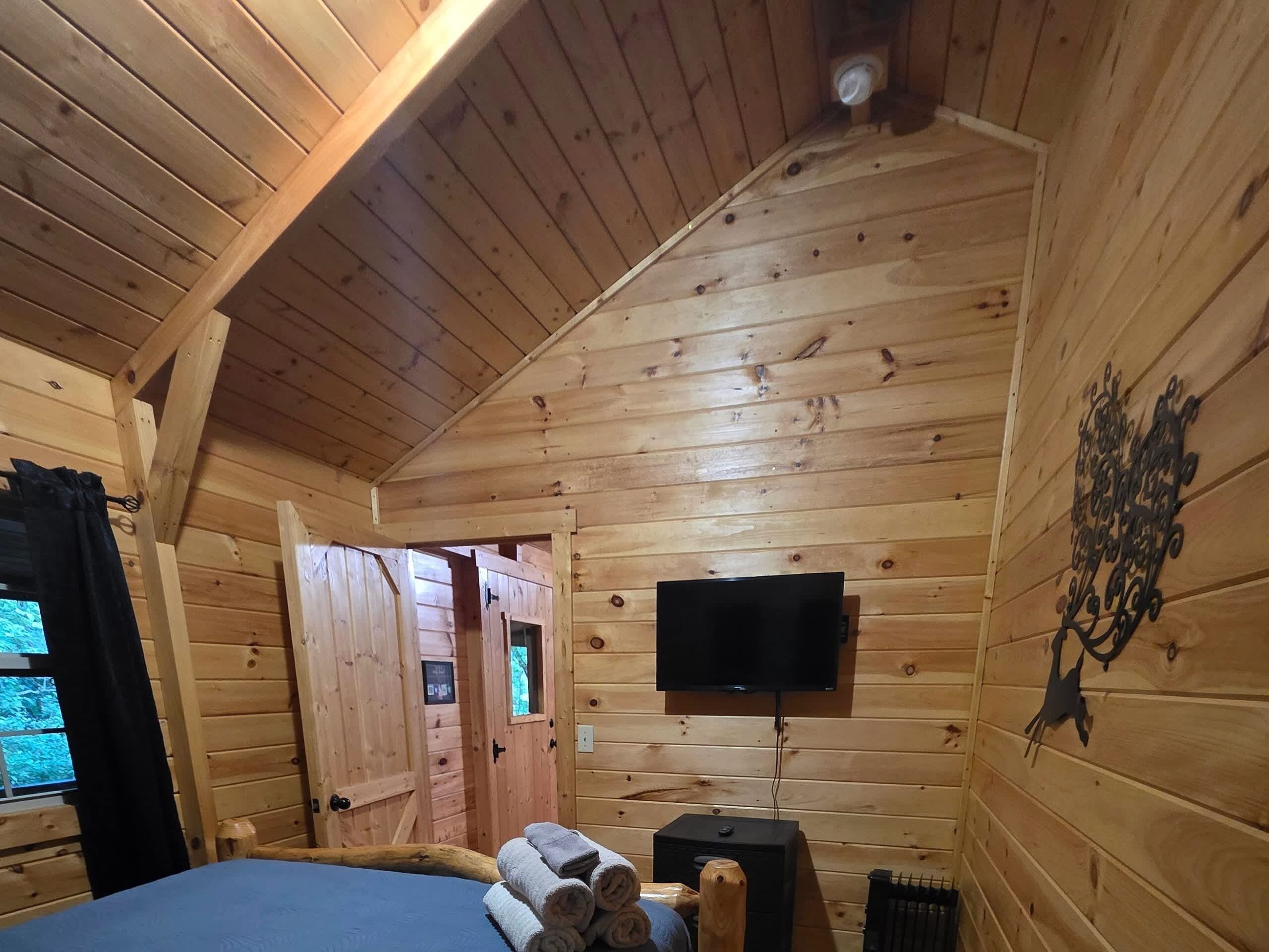 A wooden cabin room with a bed, a television, and a fireplace.