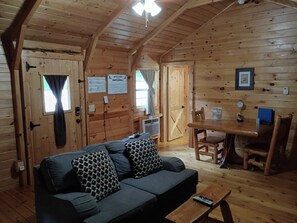 A wooden cabin interior with a sofa, a dining table, and a kitchen area.