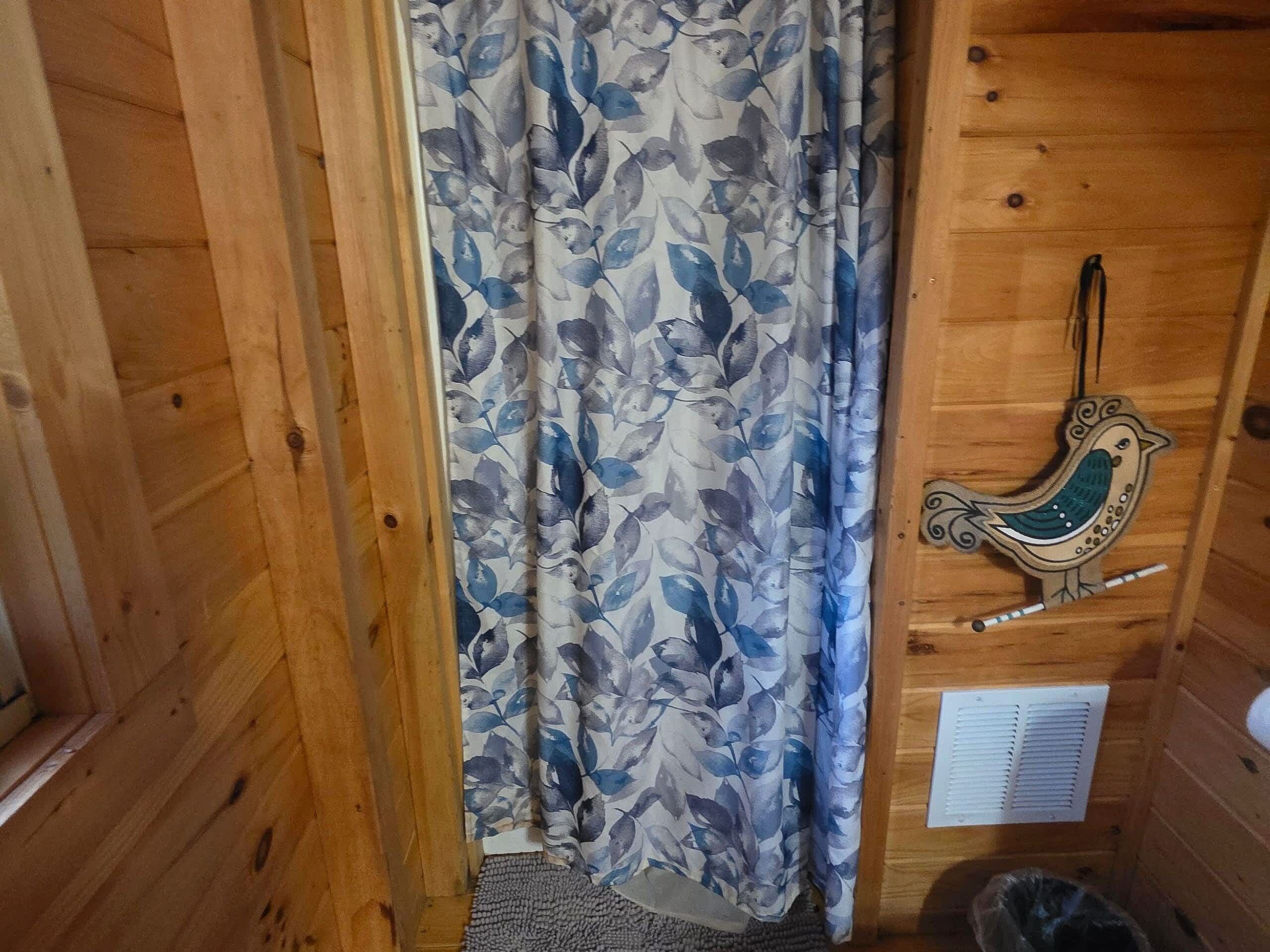Een houten blokhutinterieur met een bloemen gordijn, een decoratie in de vorm van een vogel en een ventilatie rooster.