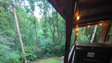 A wooden deck with a bench and a hot tub, overlooking a dense forest.