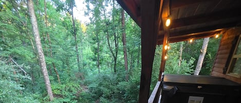 A wooden deck with a bench and a hot tub, overlooking a dense forest.