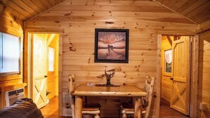 A wooden interior with a dining table and chairs, a framed picture on the wall, and a door leading to another room. - Whippoorwill at Avenwood Cabins (new straitsville)