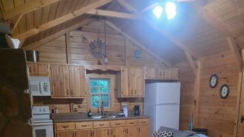 A wooden cabin interior with a kitchen, a dining area, and a living room.