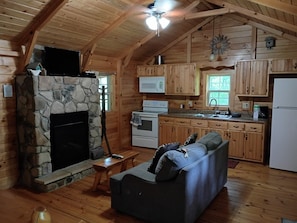 A cozy cabin interior with a stone fireplace, wooden walls, a kitchenette, and a sofa.
