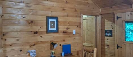 A wooden interior with a table, chairs, a framed picture, a thermostat, and a door with a sign.