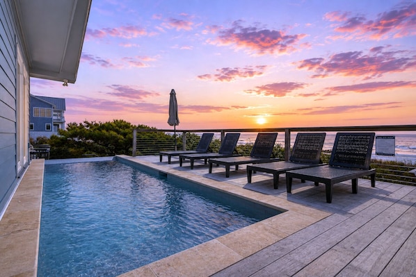 Zona de piscina con sillones de descanso y vista al atardecer sobre el océano.