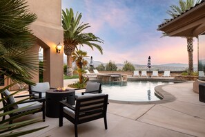 An outdoor pool area with lounge chairs, a fire pit, and a view of the mountains.