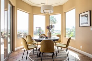 A dining area with a round table, four chairs, a vase, and a bowl of fruit.