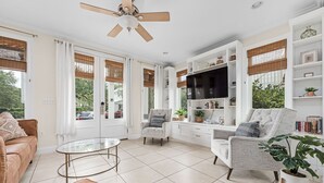 A spacious living room with a ceiling fan, a large flat-screen TV, and a comfortable seating area with a sofa and armchairs. - Escape to Blue Mountain Beach – GOLF CART, Pool, Gym & Rec Courts (Santa Rosa Beach)
