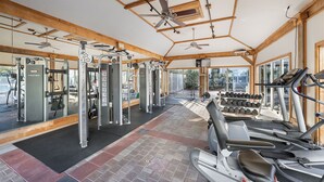 A gym with various exercise equipment, including treadmills and weight machines, under a high ceiling with wooden beams. - Escape to Blue Mountain Beach – GOLF CART, Pool, Gym & Rec Courts (Santa Rosa Beach)
