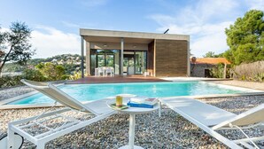 A modern house with a swimming pool, lounge chairs, and a table with books and a cup.