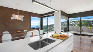 A modern kitchen with a large island, a built-in oven, and a view of a hillside.