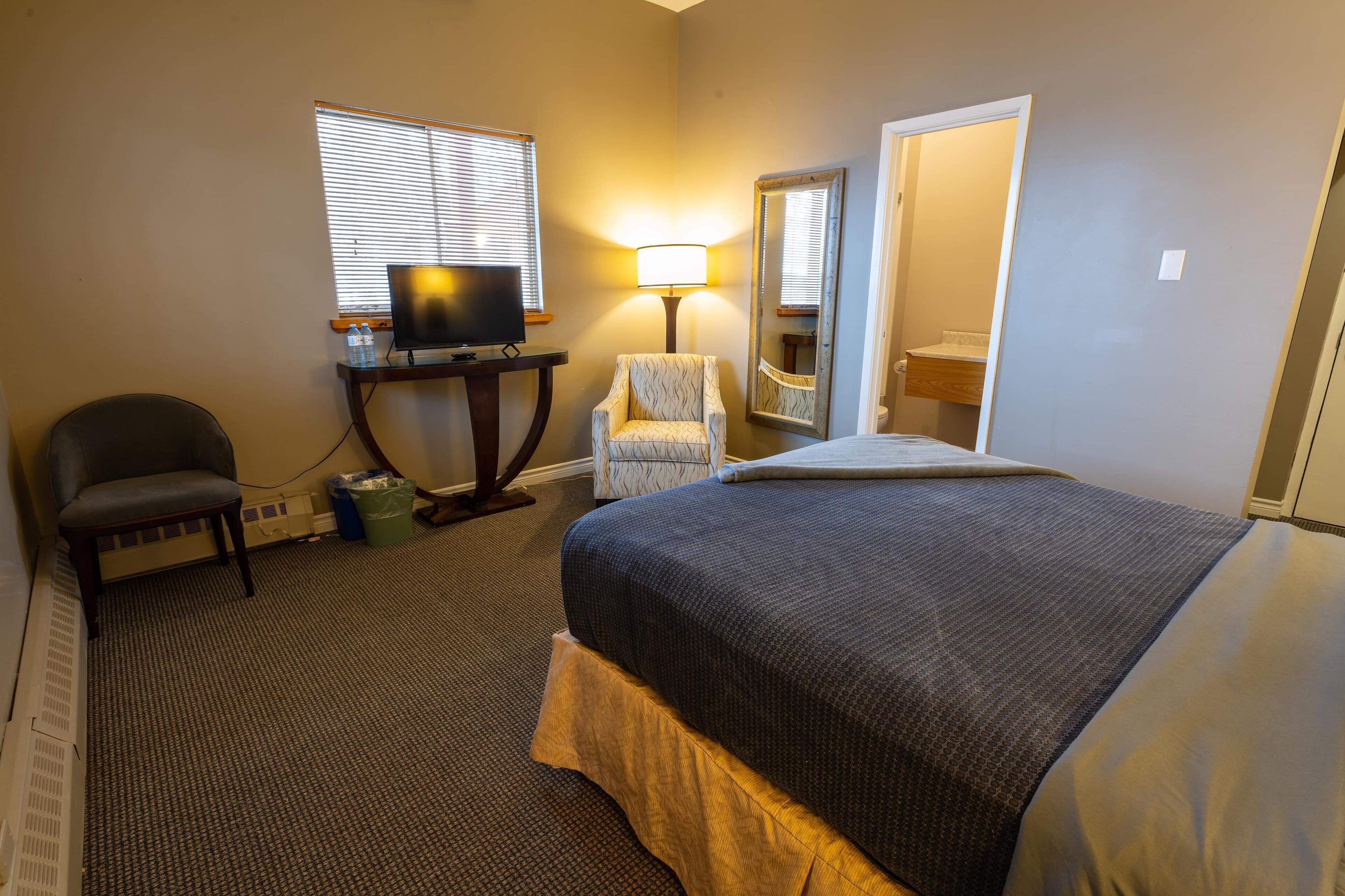 Een hotelkamer met een bed, een bureau met een televisie, een stoel, een lamp en een spiegel.