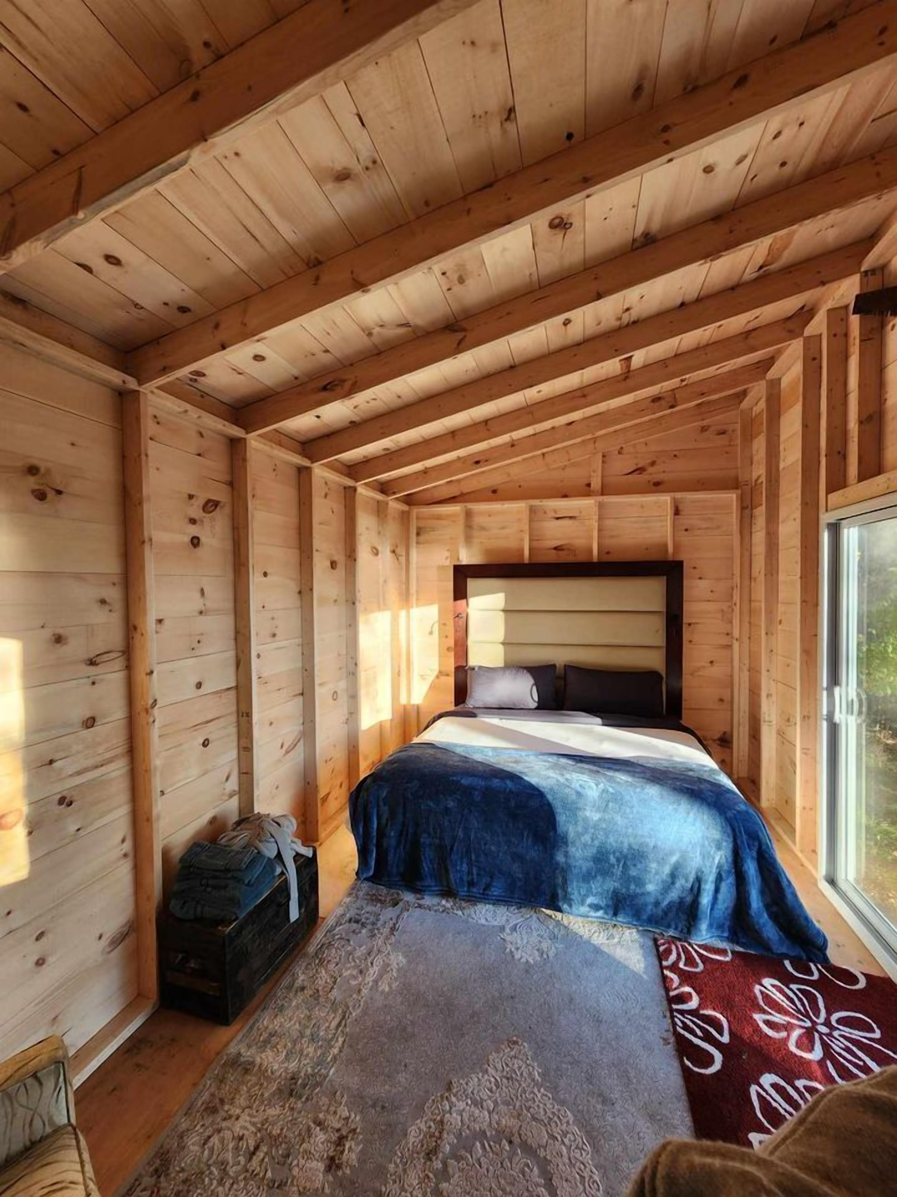 Un dormitorio tipo cabaña de madera con una cama, una ventana y un pequeño aparador.