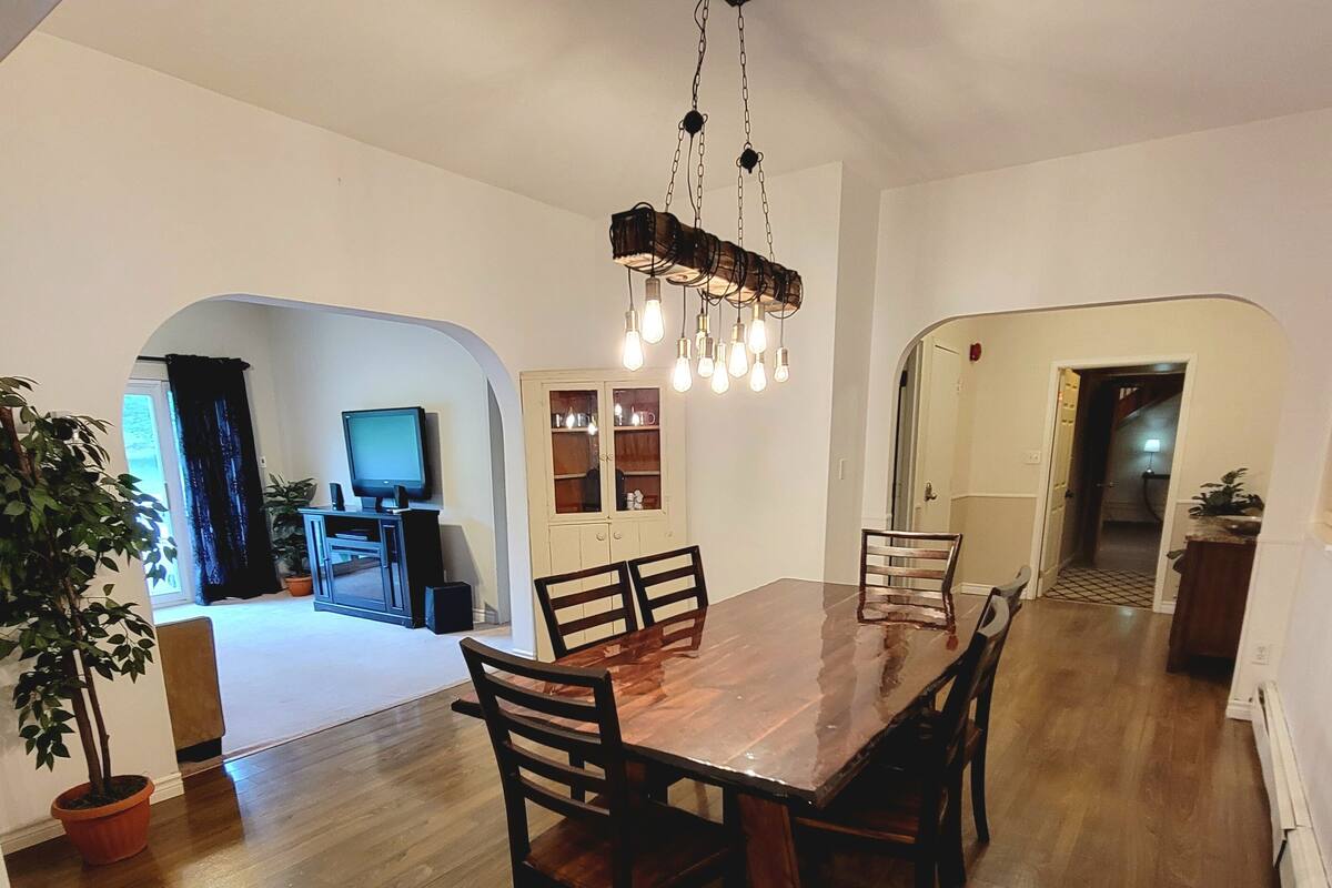 Un comedor espacioso con una mesa y sillas de madera, una araña y un televisor al fondo.