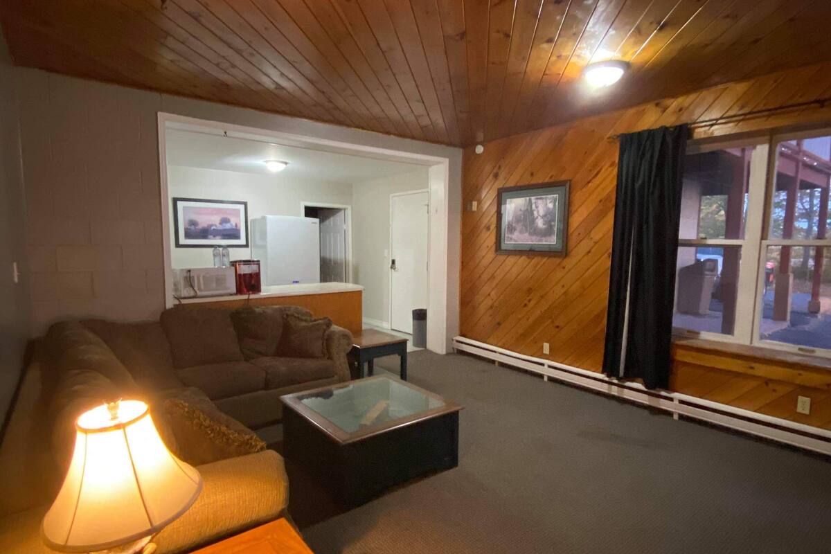Una sala de estar acogedora con techo de madera, un sofá, una mesa de centro de cristal y una lámpara.