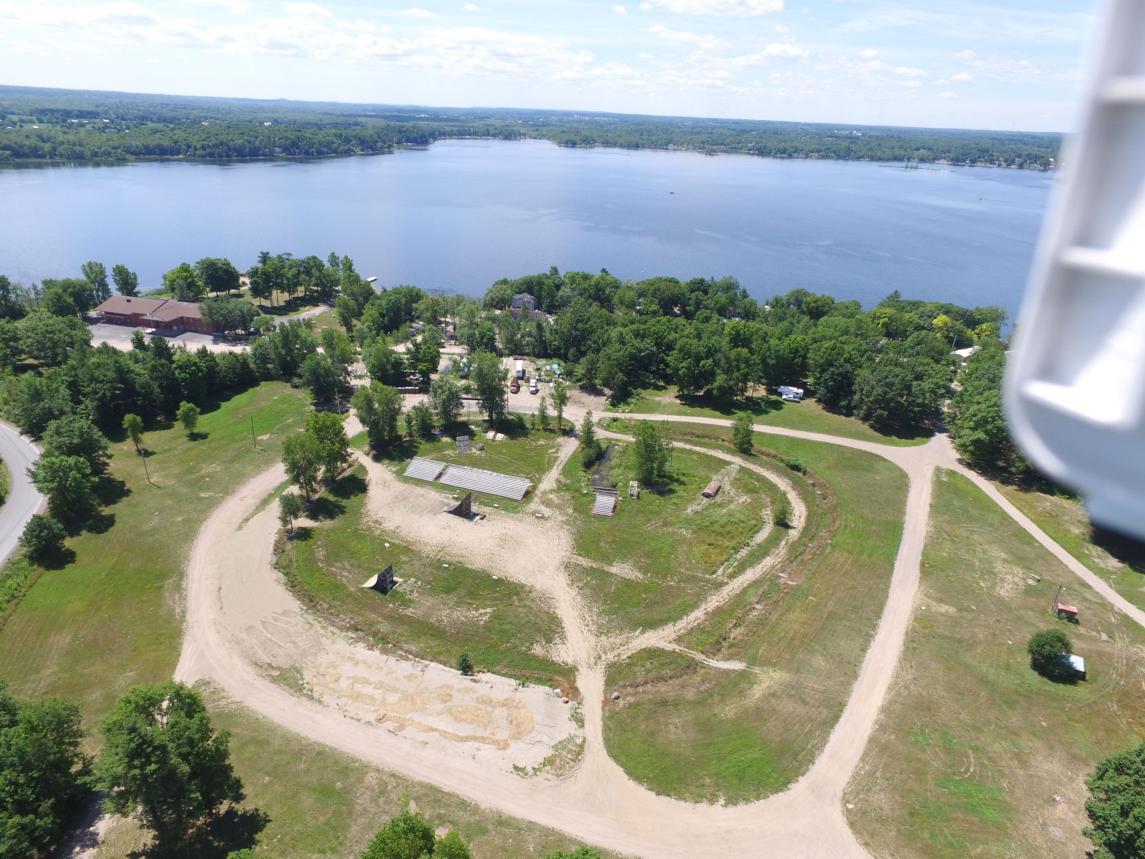 An aerial view of a property with a large lake, surrounded by trees and a few buildings.