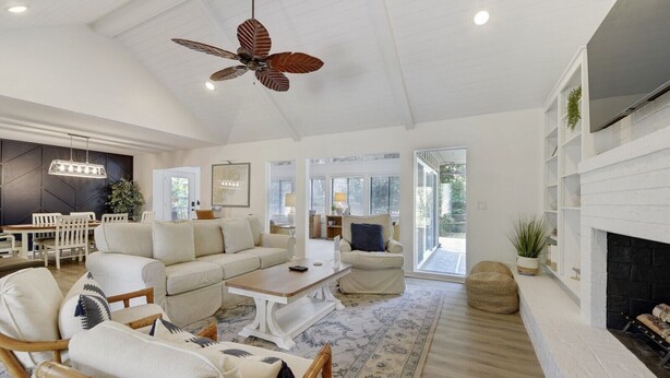 A spacious living room with a high ceiling fan, a fireplace, and a dining area with a table and chairs.
