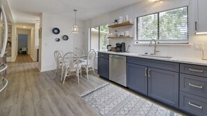 A modern kitchen with a skylight, white cabinets, and a dining area with white chairs.
