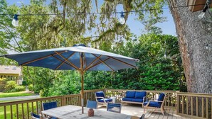 A wooden deck with a table and chairs, surrounded by a wooden railing and a large tree.