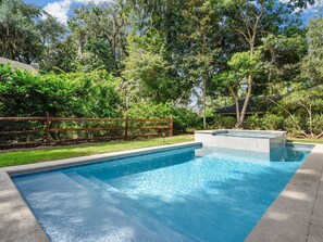 Une piscine rectangulaire entourée d’une clôture en bois, avec une végétation luxuriante en arrière-plan.