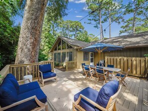 Une terrasse en bois avec des meubles d’extérieur bleus, un patio couvert et un grand arbre.